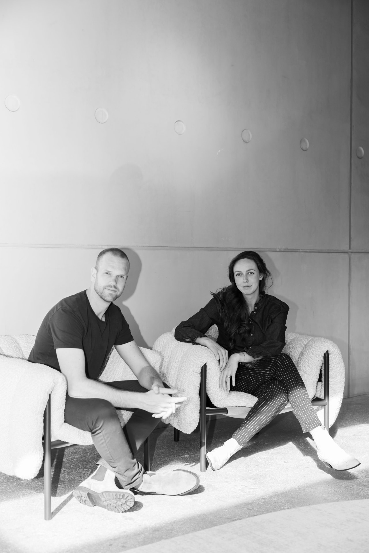 Arjan en Rosalie van MAIN in twee witte fauteuils voor een betonnen wand