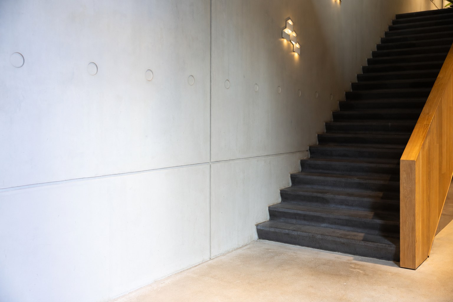 Betonnen wand met donkere trap en eikenhouten leuning